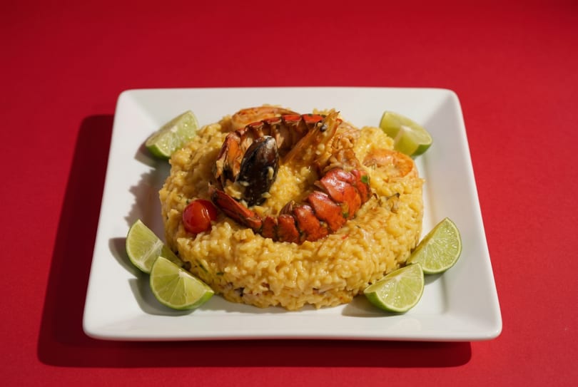 Seafood risotto with lobster, shrimp, mussels, and lime wedges on a white plate.